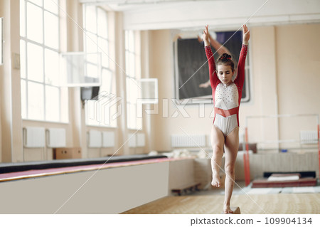 Child gymnastics balance beam. Girl gymnast athlete during an exercise horizontal bar in gymnastics competitions. Child gymnastics balance beam. Girl gymnast athlete during an exercise horizontal bar in gymnastics competitions. 109904134