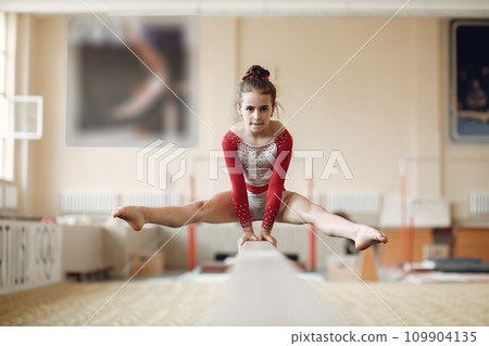 Child gymnastics balance beam. Girl gymnast athlete during an exercise horizontal bar in gymnastics competitions. 109904135