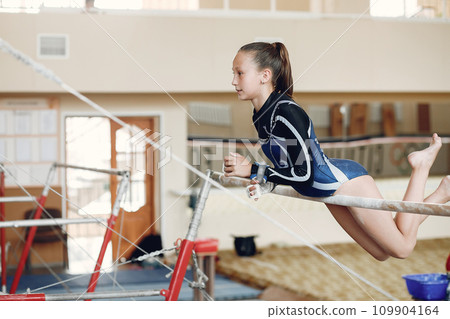 Child gymnastics balance beam. Girl gymnast athlete during an exercise horizontal bar in gymnastics competitions. Child gymnastics balance beam. Girl gymnast athlete during an exercise horizontal bar in gymnastics competitions. 109904164