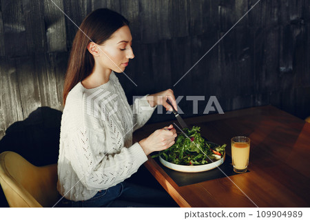 Girl eats vegetable salad. Lady sitting in a cafe. Brunette in a white sweater. Girl eats vegetable salad. Lady sitting in a cafe. Brunette in a white sweater. 109904989