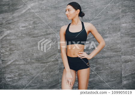 Pretty lady standing in a summer city. Brunette in a black top. Woman near gray wall Pretty lady standing in a summer city. Brunette in a black top. Woman near gray wall 109905019