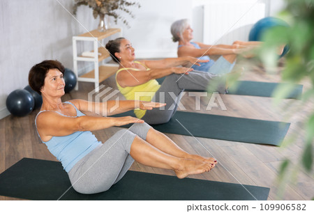 Old woman practicing boat pose of yoga in training room during fitness classes Old woman practicing boat pose of yoga in training room during fitness classes 109906582