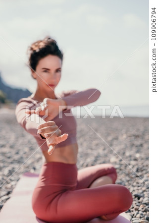 Middle aged well looking woman with black hair, fitness instructor in leggings and tops doing stretching and pilates on yoga mat near the sea. Female fitness yoga routine concept. Healthy lifestyle 109906794