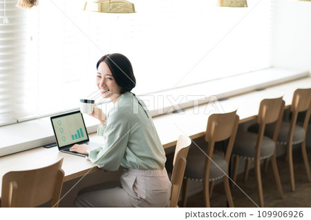 Woman looking at computer while drinking coffee at cafe 109906926