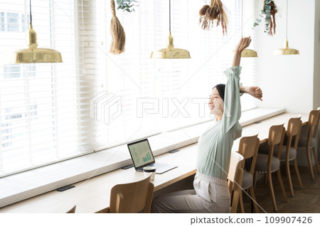 A woman stretches while working at a desk 109907426