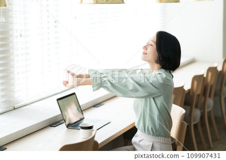 A woman stretches while working at a desk 109907431
