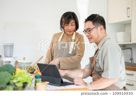 Lovely Asian couples are looking at an online recipe on a tablet and cooking in the kitchen together Lovely Asian couples are looking at an online recipe on a tablet and cooking in the kitchen together 109910930