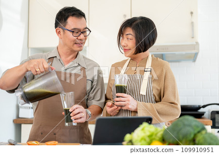 A happy Asian wife and husband are enjoying healthy green smoothie in the kitchen together 109910951