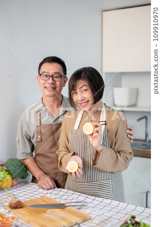A lovely Asian couple is in the kitchen, wearing apron, preparing to cook their dinner together. 109910970