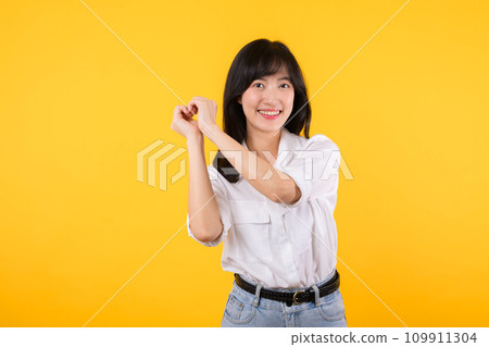 Young female healthcare. Asian woman wearing white shirt feels happy and romantic shapes heart gesture expresses tender feeling poses isolated on yellow background. People affection and care concept. 109911304