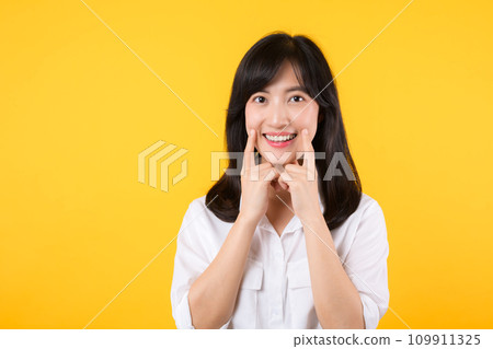Young beautiful asian woman happy smile wearing white shirt and denim jean plants over yellow isolated background smiling confident showing and pointing with fingers teeth and mouth. Dental concept. Young beautiful asian woman happy smile wearing white shirt and denim jean plants over yellow isolated background smiling confident showing and pointing with fingers teeth and mouth. Dental concept. 109911325