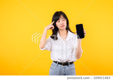 Portrait beautiful asian young woman with doubt face wearing white shirt and denim plants with smartphone isolate on yellow studio background. Disappointed in fake online news concept. Portrait beautiful asian young woman with doubt face wearing white shirt and denim plants with smartphone isolate on yellow studio background. Disappointed in fake online news concept. 109911463