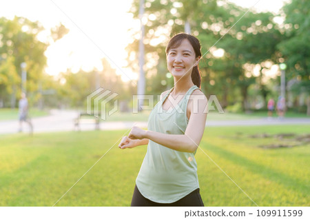 Female jogger. Fit young Asian woman with green sportswear stretching muscle in park before running and enjoying a healthy outdoor. Fitness runner girl in public park. Wellness being concept 109911599