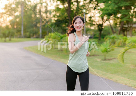 Fit Asian young woman jogging in park smiling happy running and enjoying a healthy outdoor lifestyle. Female jogger. Fitness runner girl in public park. healthy lifestyle and wellness being concept 109911730
