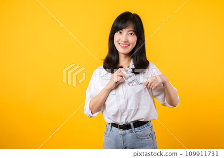 Captivating image of Asian young woman wearing white shirt and denim jeans, confidently holding cash from her shirt pocket. Fashion meets financial empowerment. Perfect for finance and fashion themes. 109911731