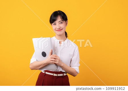 Portrait beautiful young asian woman enterpriser happy smile wearing white shirt and red plants showing confident body language gesture and holding laptop isolation on yellow background. 109911912