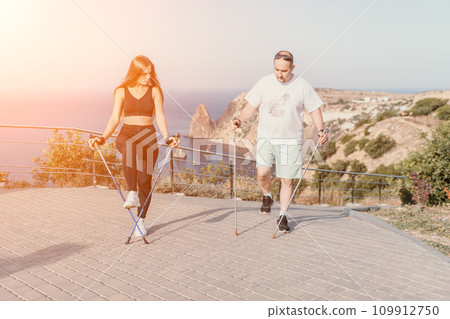 Happy Middle aged couple or friends practicing nordic walking in park near sea. Mature couple with trekking poles walking, practicing Nordic walking outdoors. Aging youthfully and sport concept Happy Middle aged couple or friends practicing nordic walking in park near sea. Mature couple with trekking poles walking, practicing Nordic walking outdoors. Aging youthfully and sport concept 109912750