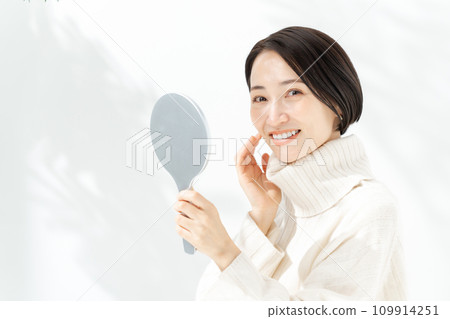 A woman checking her skin with a hand mirror 109914251