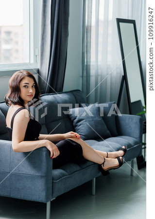 Young beautiful brunette girl in a black dress sitting on the sofa 109916247