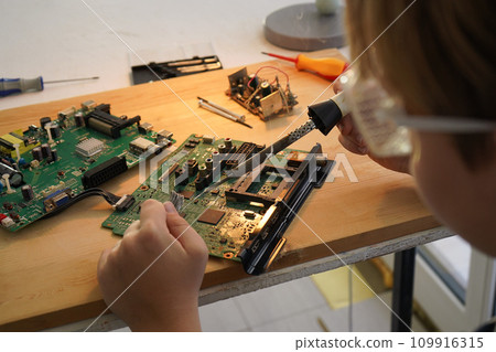 Father with his son spend time together. Close-up of a man teaching his boy at home to solder computer spare parts. Education moment during parenthood. Togetherness concept. 109916315