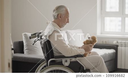 Lonely old man in wheelchair holding teddy bear, missing family in a retirement home Lonely old man in wheelchair holding teddy bear, missing family in a retirement home 109916682