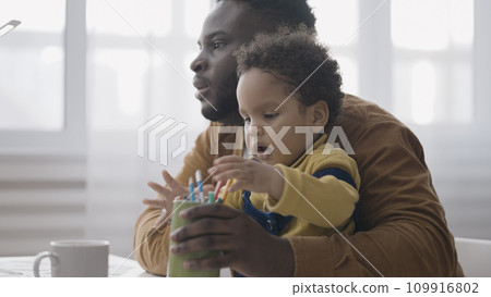 Caring dad having online video call and holding baby on lap, working parent challenges 109916802