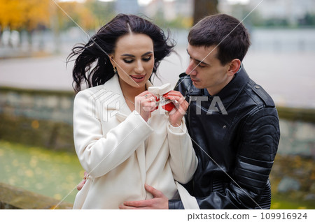 A pregnant woman sits on her husband's lap and holds small baby socks in her hands. A pregnant woman sits on her husband's lap and holds small baby socks in her hands. 109916924