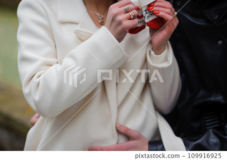 A pregnant woman sits on her husband's lap and holds small baby socks in her hands. A pregnant woman sits on her husband's lap and holds small baby socks in her hands. 109916925
