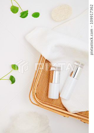 Two cosmetic bottles with luxurious design and a towel in a rattan basket, surrounded by fresh pennywort leaves. Minimalist white background with delicate cosmetics mockup. Two cosmetic bottles with luxurious design and a towel in a rattan basket, surrounded by fresh pennywort leaves. Minimalist white background with delicate cosmetics mockup. 109917362