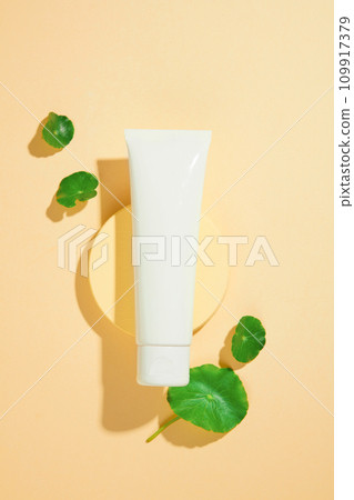 A tube of cosmetics is displayed on a round platform, surrounded by fresh pennywort leaves. Centella has the ability to inhibit the formation of melanin, reduce dark spots and even skin tone. 109917379