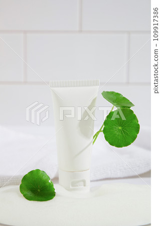 Centella asiatica leaves decorate around a tube of unbranded facial cleanser with a white background. Gotu kola is considered a miracle drug to improve dark spots and brighten. 109917386