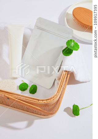 A mask sheet and an unbranded white tube are placed in a rattan basket on a white background with the green color of pennywort leaves. Branding a vegan cosmetics. 109917395