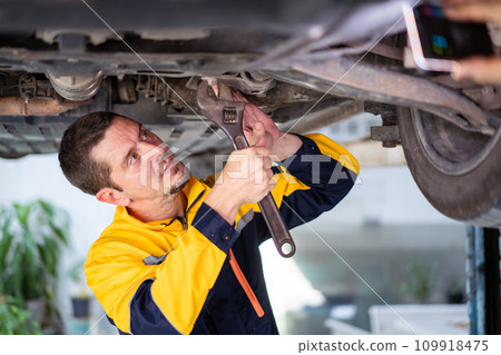 Professional caucasian white automobile technician inspecting and checking under - suspension of a vehicle in garage. Professional caucasian white automobile technician inspecting and checking under - suspension of a vehicle in garage. 109918475