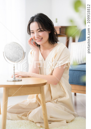 一位年輕可愛的女人在鏡子裡檢查皮膚狀況和化妝時迷人地微笑著，在室內植物、肖像前模糊 109918812