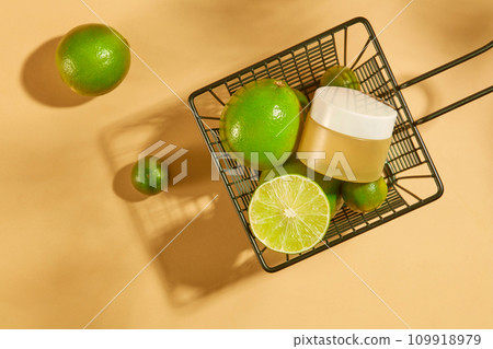 An unlabeled cosmetic jar is placed in an iron basket with fresh lemons and kumquats. The acid in lemon can reduce facial scars. Mockup for vegan cosmetics advertisement. 109918979