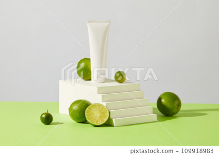 Front view of a white tube placed on a podium with fresh lemon and kumquat on a pastel background. Cosmetics advertising with sophisticated space. Cosmetics with natural extracts. 109918983