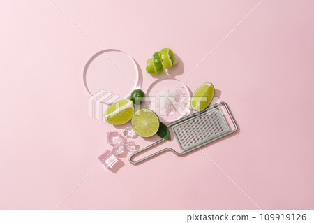 Sea salt is displayed on a glass platform, surrounded by ice and fresh lemons, a grater on a pastel pink background. Lemon is an effective skin beautifying food, treating acne and dark scars 109919126