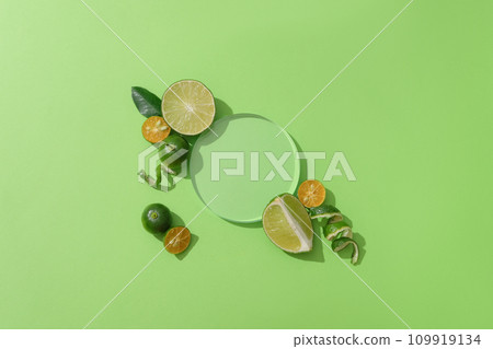 On a green backdrop, a clear glass podium is surrounded by fresh lemons and kumquats-an inviting display space for showcasing natural products. On a green backdrop, a clear glass podium is surrounded by fresh lemons and kumquats-an inviting display space for showcasing natural products. 109919134