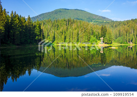 landscape of a synevyr lake in summer. nature scenery with reflection of a coniferous forest on the mountain hillside beneath a blue sky with clouds on a sunny day. popular travel destination of landscape of a synevyr lake in summer. nature scenery with reflection of a coniferous forest on the mountain hillside beneath a blue sky with clouds on a sunny day. popular travel destination of 109919554
