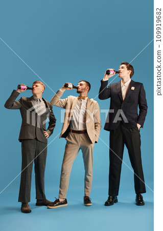 Handsome men in stylish suits, friends attending party, drinking beer against blue background. Wedding day 109919682
