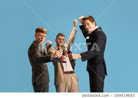 Happy stylish young me, groom's friends cheerfully celebrating, drinking beer against blue background Happy stylish young me, groom's friends cheerfully celebrating, drinking beer against blue background 109919683