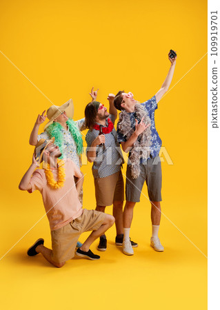 Group of cheerful friends, men in stylish clothes travelling to vacation, taking photo together against yellow background 109919701