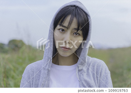 Upper body portrait of a young woman wearing a hoodie standing on a path along the bank Upper body portrait of a young woman wearing a hoodie standing on a path along the bank 109919763