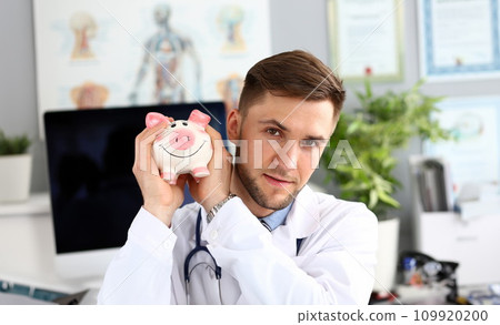 Doctor posing with piggy bank Doctor posing with piggy bank 109920200