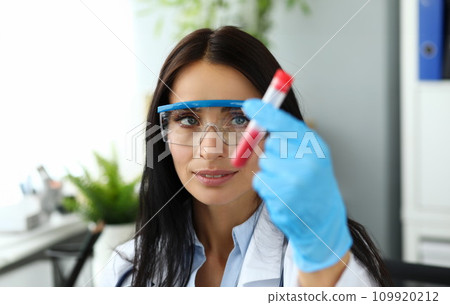 Beautiful woman wearing protective glasses holding test tube 109920212