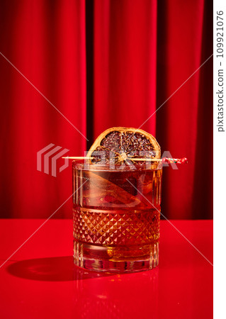 Close-up photo of cocktail with ice cubes, elegancy garnished orange slice served on red bar counter in restaurant. Concept of celebrating. Close-up photo of cocktail with ice cubes, elegancy garnished orange slice served on red bar counter in restaurant. Concept of celebrating. 109921076