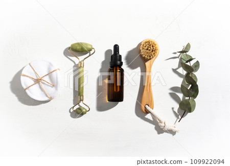 Face massage roller, serum, cotton pads and brush on light white background. Face massage roller, serum, cotton pads and brush on light white background. 109922094