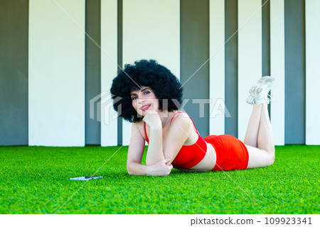 Creative bright girl in summer shorts lies on the lawn with a phone Creative bright girl in summer shorts lies on the lawn with a phone 109923341