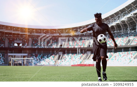 African American man playing football on the stadium field. A man runs with a soccer ball across the field. African American man playing football on the stadium field. A man runs with a soccer ball across the field. 109924955