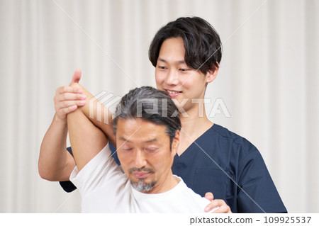 一位年輕的脊椎按摩師正在為一名男子進行治療 一位年輕的脊椎按摩師正在為一名男子進行治療 109925537